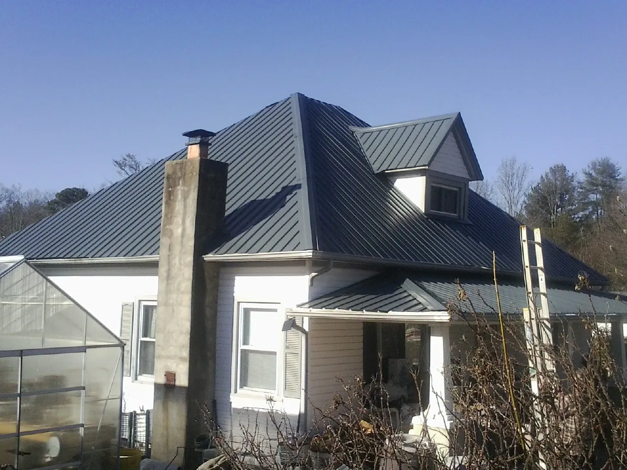 Dark blue standing seam metal roof on a white farmhouse with dormer — Slate & Tile Roof Repair by Roofing Brothers in Dazey