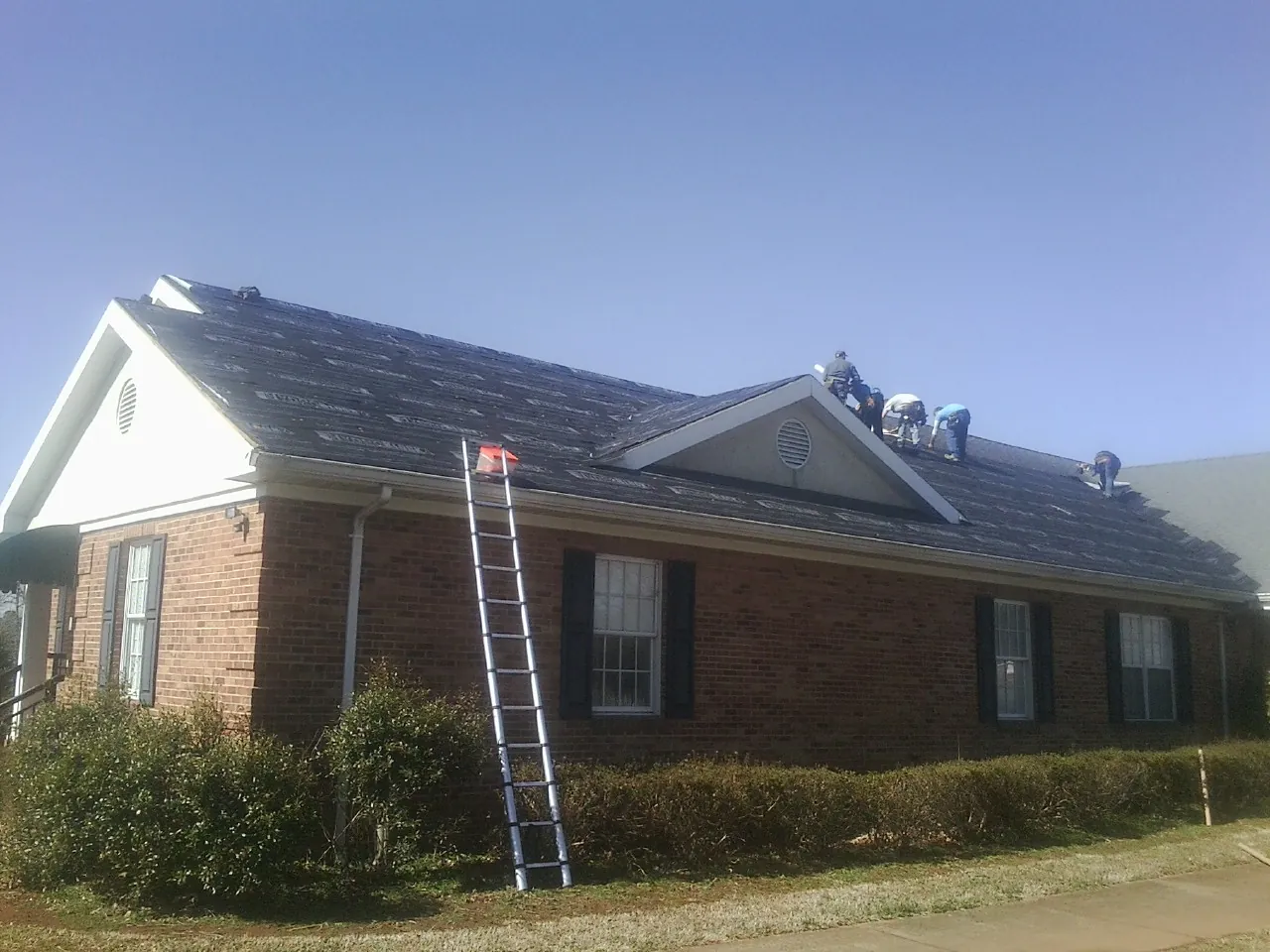 Crew tearing shingles off a brick ranch roof with a ladder set — Metal Roof Repair work by our crew in Dazey