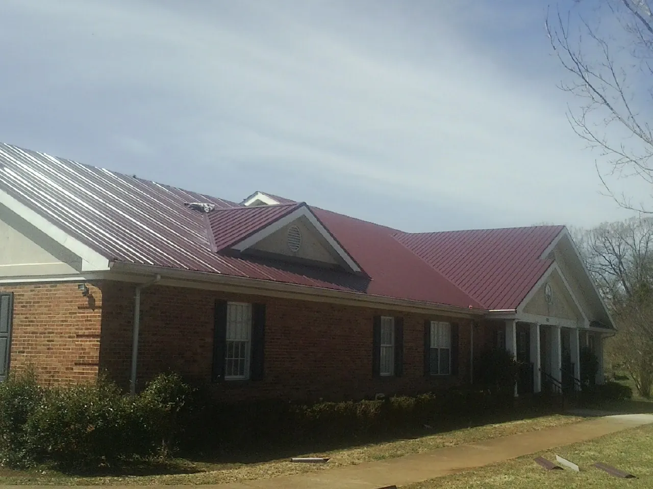 Red metal roof with gabled entries on a long brick building, from a Hail Damage Roof Repair job in Dazey