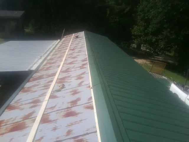 Old rusted panels beside newly installed green metal roofing — Wind Damage Roof Repair by Roofing Brothers in Dazey