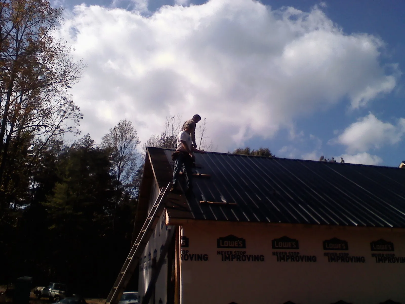 Roofer fastening dark metal panels high against a cloudy sky, from a Roof Inspection job in Dazey