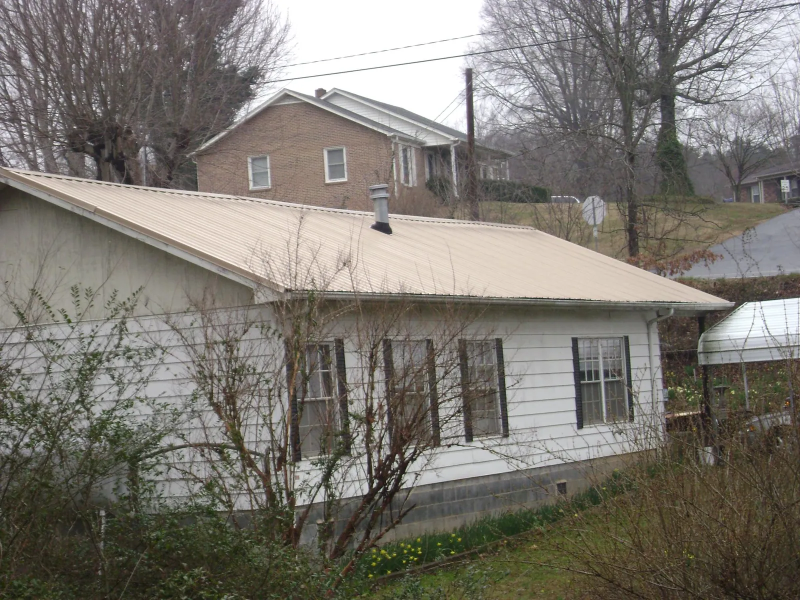 Tan metal roof on a white sided house set into a hillside — Commercial Roofing by Roofing Brothers in Dazey